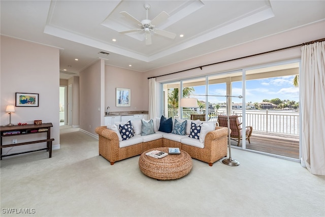 carpeted living room with sink, ceiling fan, a raised ceiling, and crown molding