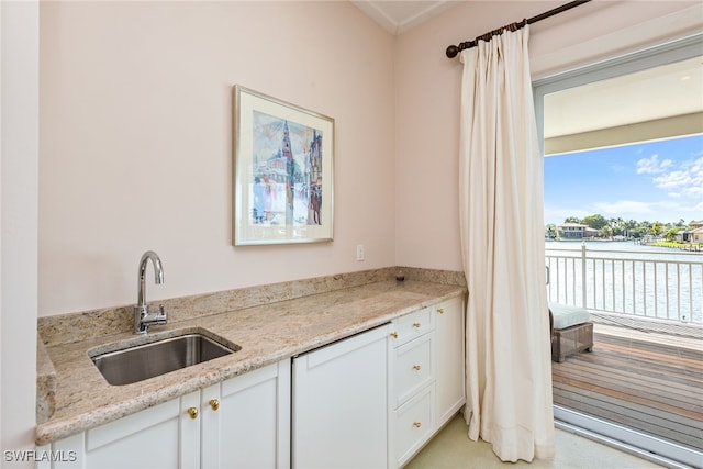 kitchen with white cabinetry, sink, a water view, light stone countertops, and light colored carpet