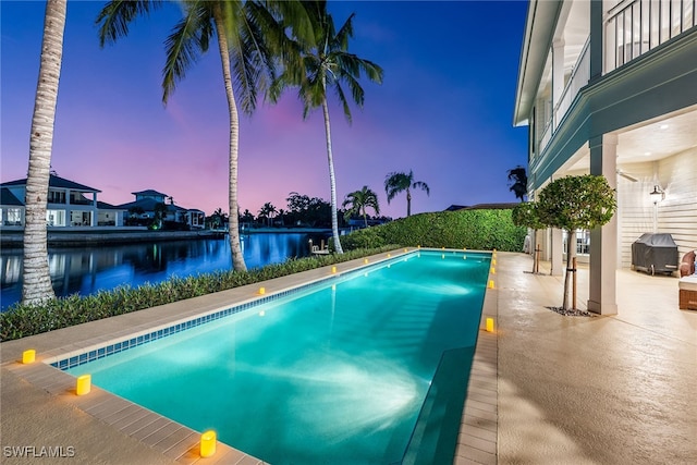 pool at dusk with a water view and a patio area