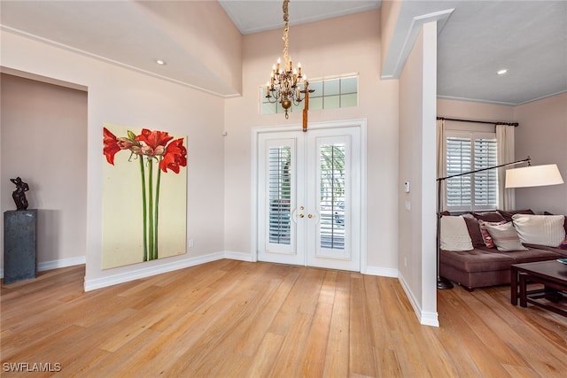 entrance foyer with ornamental molding, french doors, light hardwood / wood-style flooring, and a notable chandelier