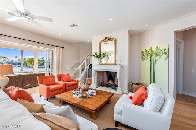 living room featuring ceiling fan, a water view, light hardwood / wood-style floors, and crown molding