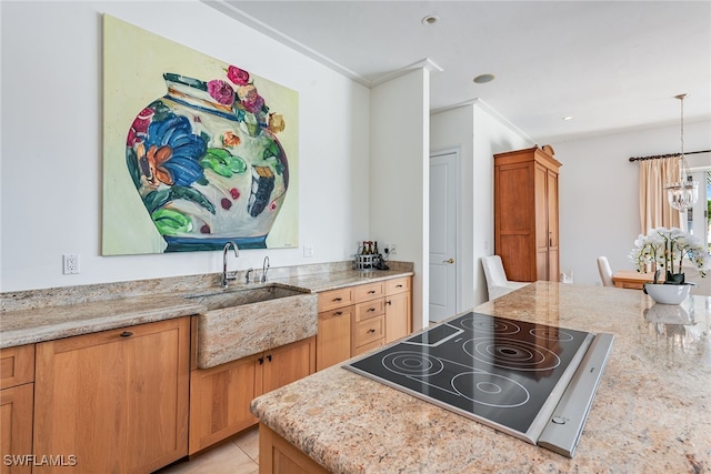 kitchen featuring black electric cooktop, light stone counters, sink, ornamental molding, and decorative light fixtures