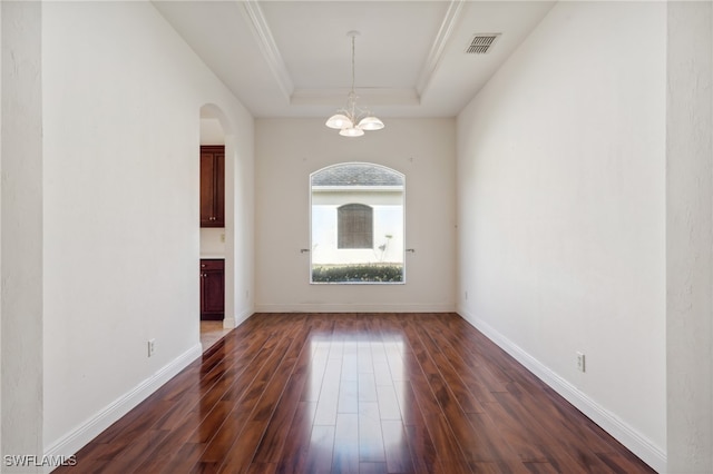 empty room with a chandelier, ornamental molding, a tray ceiling, and dark wood-type flooring