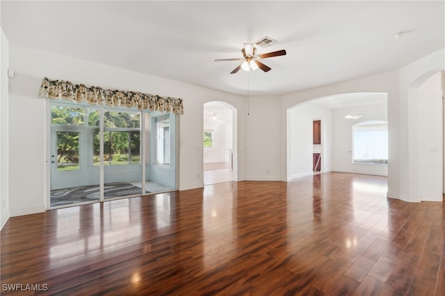 empty room featuring ceiling fan with notable chandelier, dark hardwood / wood-style flooring, and a wealth of natural light