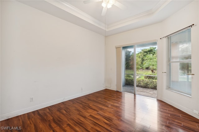 empty room featuring a raised ceiling, ceiling fan, dark wood-type flooring, and ornamental molding