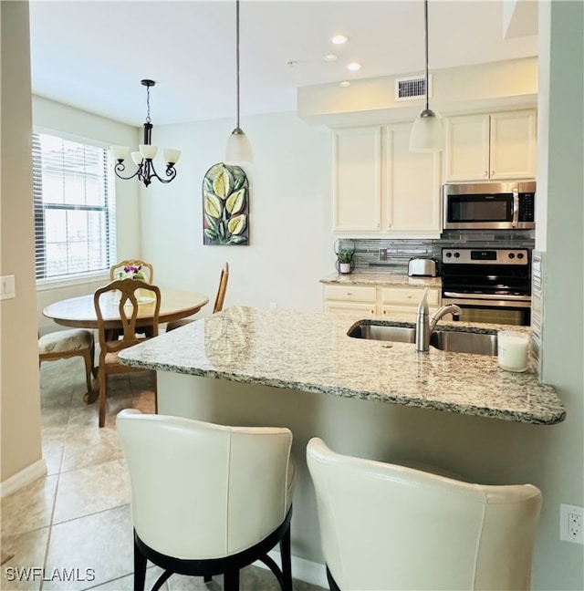 kitchen with light stone counters, appliances with stainless steel finishes, tasteful backsplash, a kitchen bar, and a chandelier