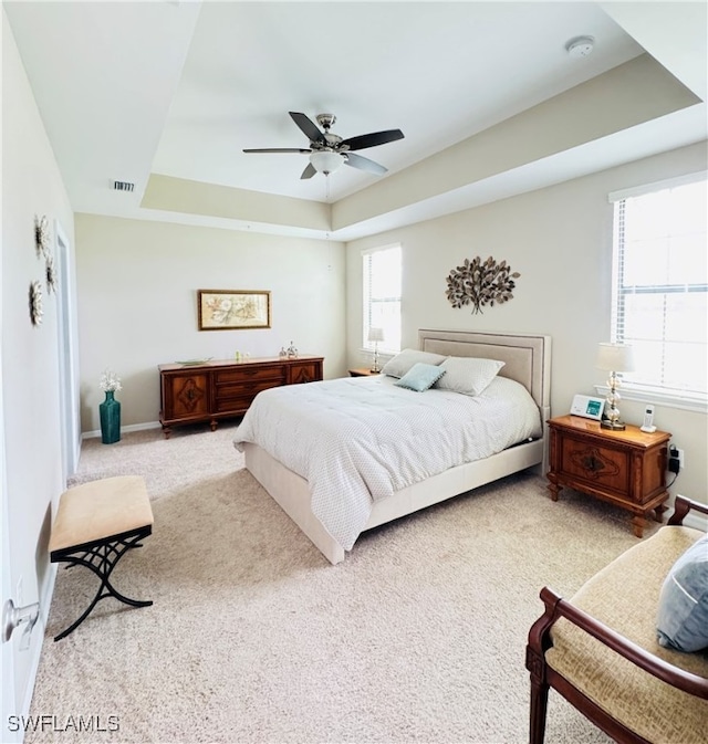 bedroom featuring ceiling fan, a raised ceiling, and light colored carpet