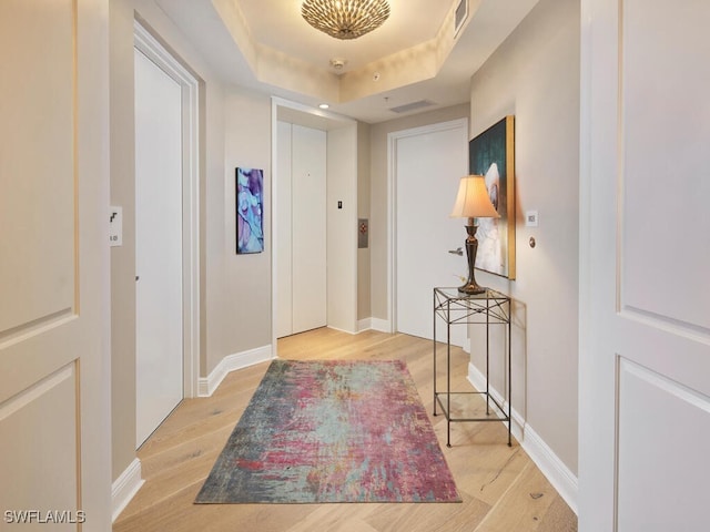 hall with light wood-type flooring and a tray ceiling