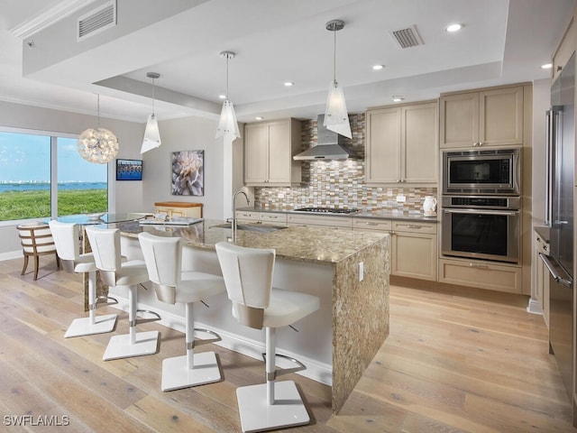 kitchen with built in appliances, sink, an island with sink, light hardwood / wood-style flooring, and wall chimney range hood