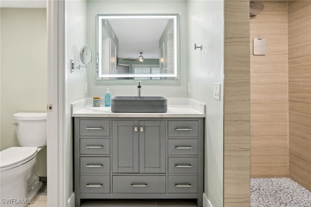 bathroom featuring a tile shower, vanity, toilet, and ceiling fan