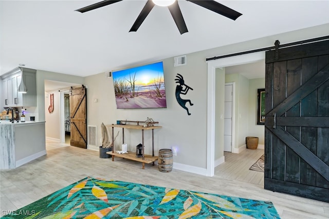 interior space featuring a barn door, light hardwood / wood-style flooring, ceiling fan, and sink