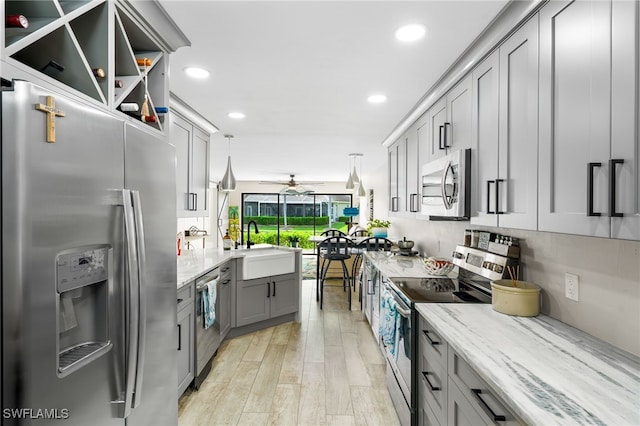 kitchen with ceiling fan, gray cabinets, light wood-type flooring, appliances with stainless steel finishes, and decorative light fixtures