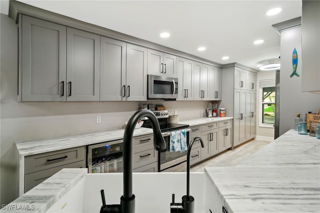 kitchen with appliances with stainless steel finishes, light hardwood / wood-style floors, beverage cooler, and gray cabinetry