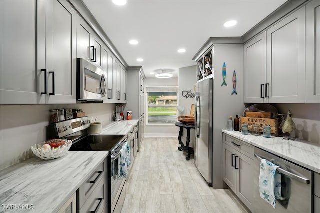 kitchen featuring gray cabinetry, light stone counters, stainless steel appliances, and light hardwood / wood-style flooring