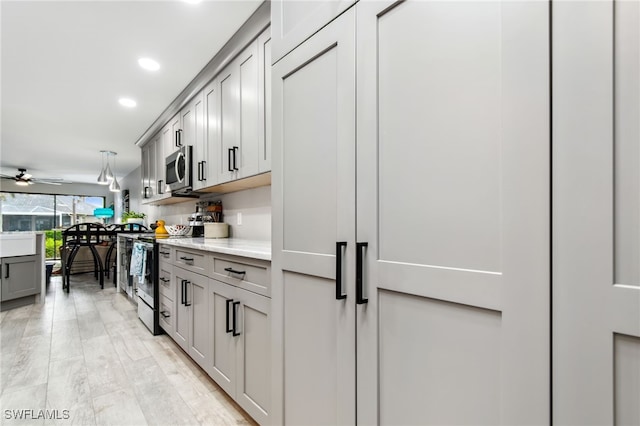 kitchen with light stone countertops, stainless steel appliances, ceiling fan, light hardwood / wood-style flooring, and gray cabinets