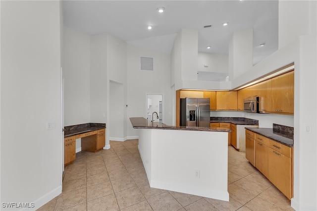 kitchen featuring a kitchen island with sink, a towering ceiling, stainless steel appliances, and light tile patterned floors