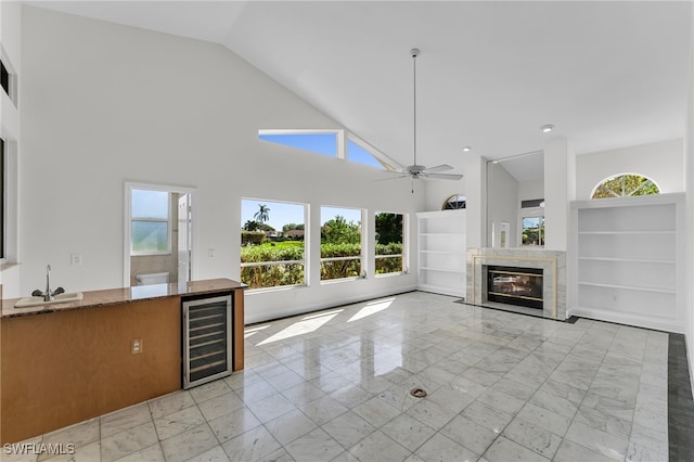 unfurnished living room with high vaulted ceiling, sink, wine cooler, ceiling fan, and a premium fireplace