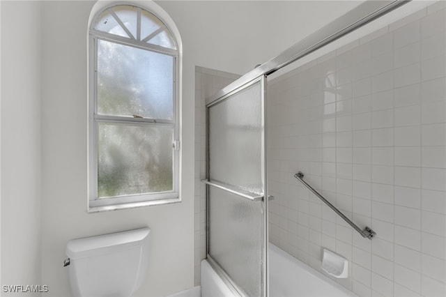 bathroom with combined bath / shower with glass door, toilet, and a wealth of natural light