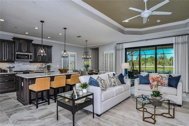 living room featuring sink, ceiling fan with notable chandelier, and crown molding