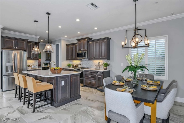 kitchen featuring tasteful backsplash, crown molding, appliances with stainless steel finishes, decorative light fixtures, and a kitchen breakfast bar