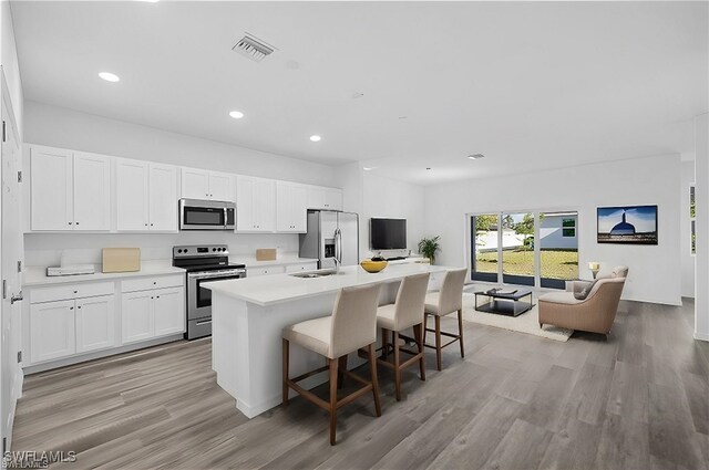 kitchen featuring light hardwood / wood-style floors, a kitchen island with sink, a kitchen breakfast bar, white cabinetry, and appliances with stainless steel finishes