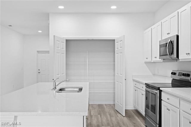 kitchen with a center island with sink, stainless steel appliances, light wood-type flooring, white cabinetry, and sink