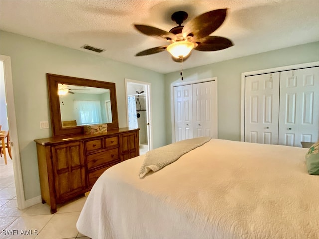 tiled bedroom featuring ensuite bath, a textured ceiling, ceiling fan, and two closets