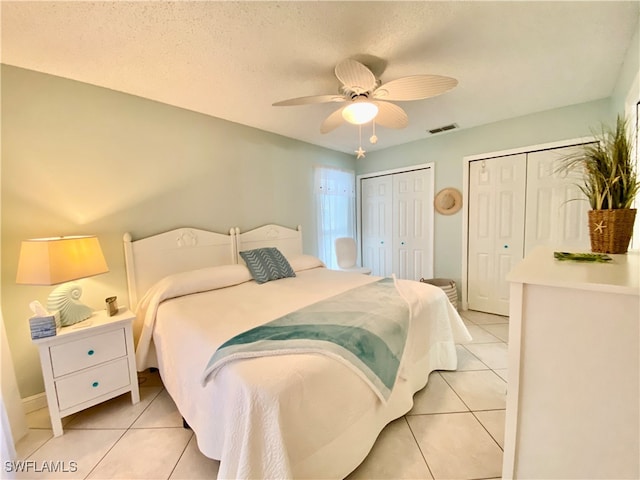 bedroom featuring two closets, a textured ceiling, light tile patterned floors, and ceiling fan