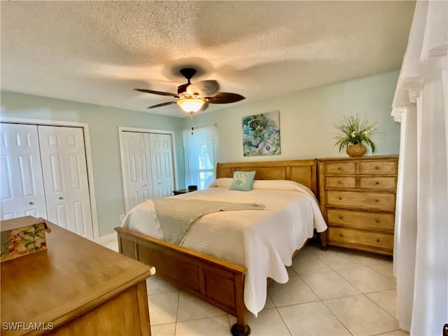 bedroom with a textured ceiling, multiple closets, ceiling fan, and light tile patterned floors