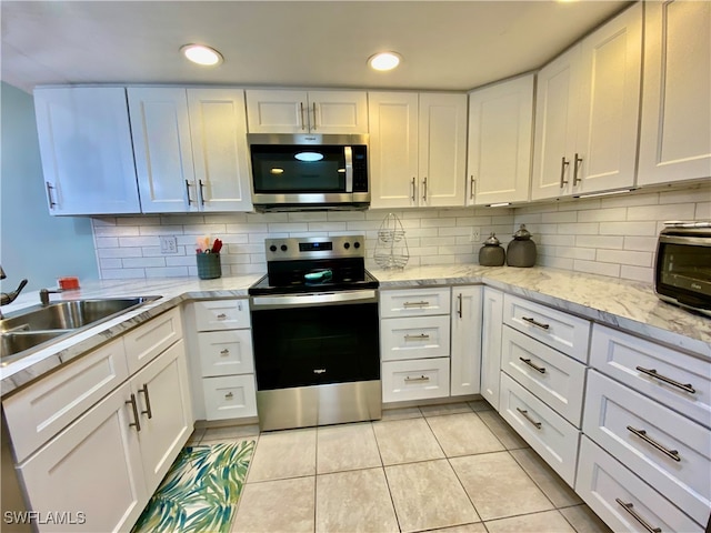 kitchen featuring stainless steel appliances, white cabinetry, light tile patterned floors, and decorative backsplash