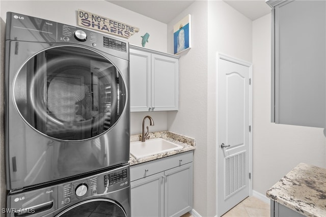 laundry area featuring sink, light tile patterned flooring, cabinets, and stacked washer and clothes dryer