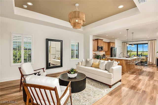 living room with sink, light wood-type flooring, and a tray ceiling