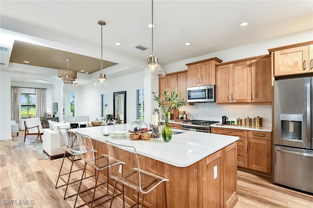 kitchen with tasteful backsplash, a center island with sink, stainless steel appliances, light wood-type flooring, and pendant lighting