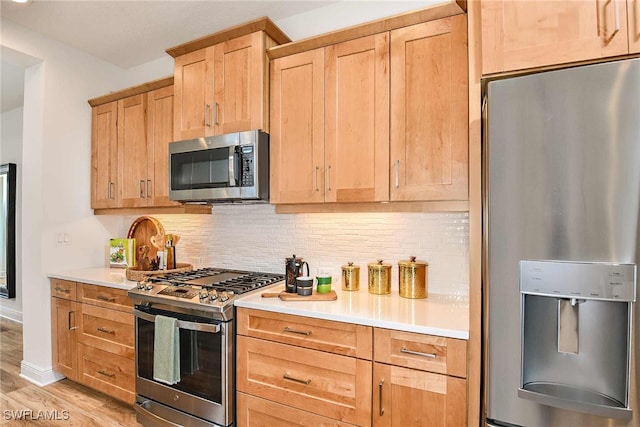 kitchen featuring appliances with stainless steel finishes, light brown cabinetry, tasteful backsplash, and light hardwood / wood-style flooring