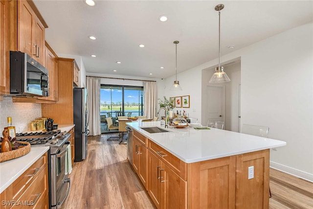 kitchen featuring stainless steel appliances, pendant lighting, sink, light hardwood / wood-style floors, and a kitchen island with sink