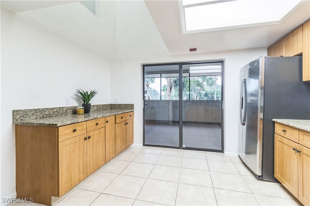 kitchen with stainless steel refrigerator with ice dispenser, dark stone counters, a skylight, and light tile patterned flooring