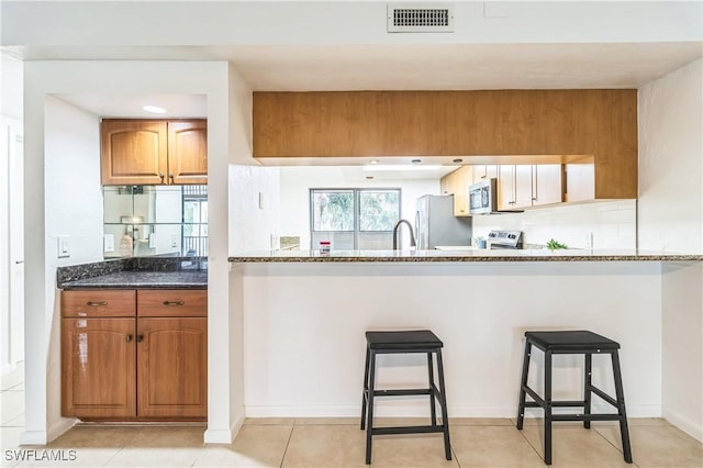 16448 Timberlakes Dr Unit 202, Fort Myers, FL 33908 - kitchen featuring stainless steel appliances, dark stone counters, a kitchen breakfast bar, and brown cabinetry