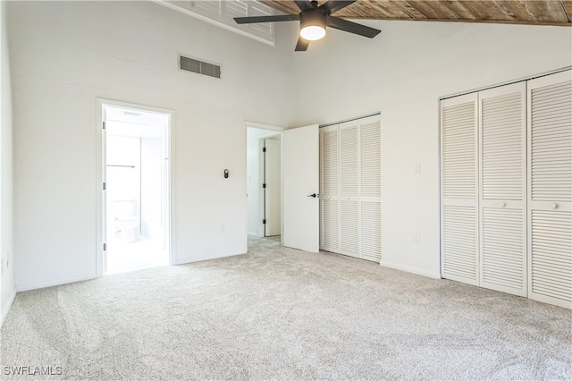 unfurnished bedroom with ensuite bath, carpet flooring, multiple closets, wooden ceiling, and ceiling fan