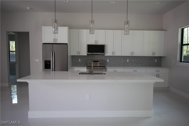 kitchen featuring stainless steel appliances, a center island with sink, backsplash, decorative light fixtures, and white cabinets