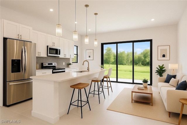 kitchen with a sink, an island with sink, a breakfast bar, appliances with stainless steel finishes, and white cabinetry