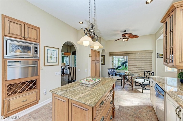 kitchen featuring light stone countertops, appliances with stainless steel finishes, ceiling fan, a center island, and hanging light fixtures