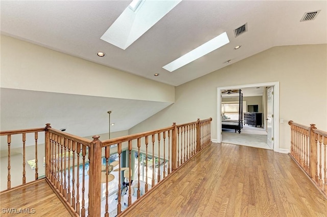 hallway with vaulted ceiling with skylight and light hardwood / wood-style flooring