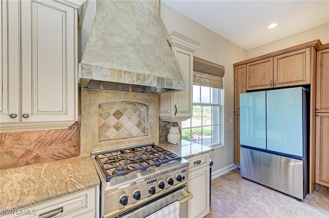 kitchen with decorative backsplash, light stone counters, wall chimney range hood, and stainless steel appliances