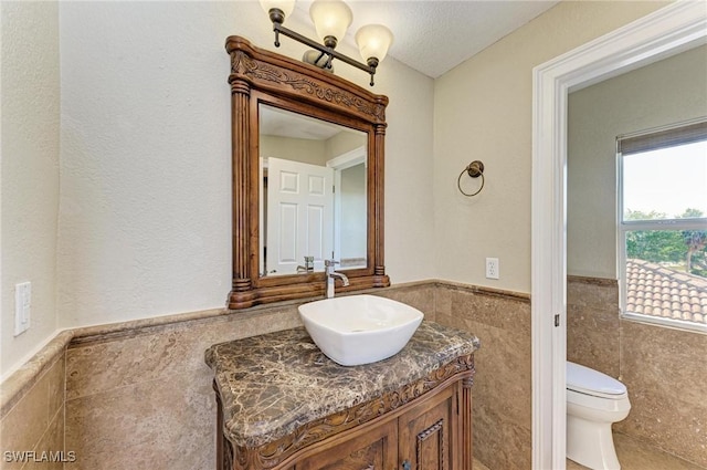 bathroom featuring a textured ceiling, vanity, toilet, and tile walls