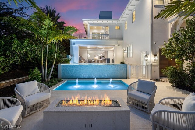 pool at dusk featuring pool water feature, a patio, and an outdoor fire pit