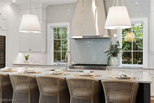 kitchen with a wealth of natural light, white cabinetry, and wall chimney range hood