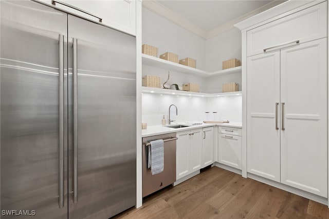 kitchen featuring ornamental molding, stainless steel appliances, sink, light hardwood / wood-style floors, and white cabinetry