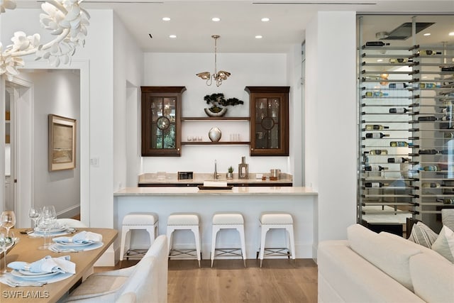 bar with an inviting chandelier, wood-type flooring, sink, decorative light fixtures, and dark brown cabinetry