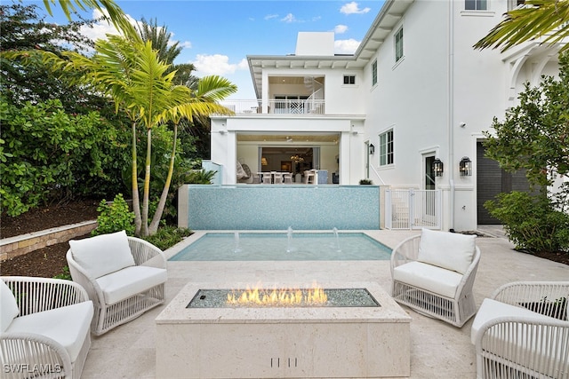 rear view of house featuring a fire pit, a fenced in pool, pool water feature, a balcony, and a patio