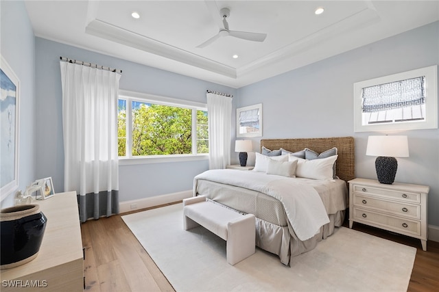 bedroom with hardwood / wood-style flooring, ceiling fan, and a tray ceiling